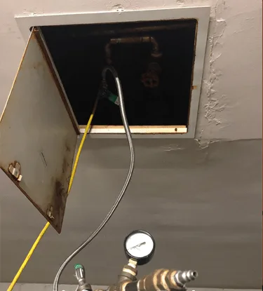 Pressure gauge connected to a new condominium riser through an access panel during an air test